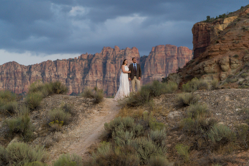 A bride and groom standing on a trail in zion national park.