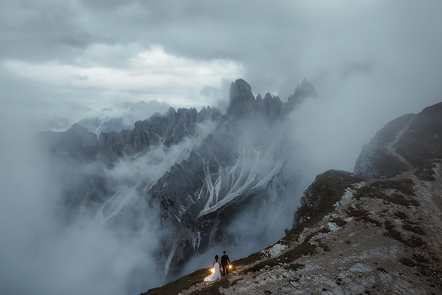 A person standing on top of a mountain with clouds in the background.